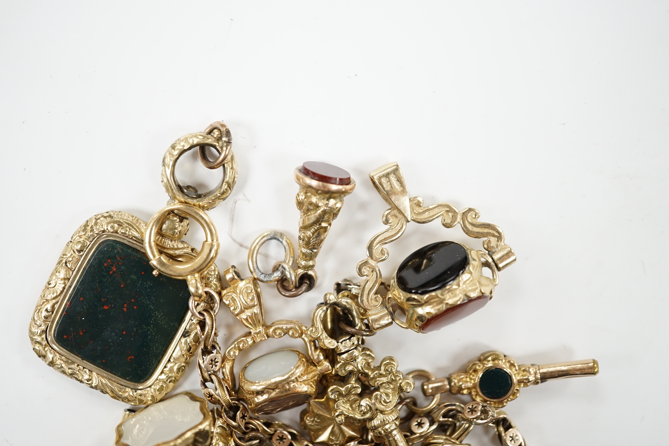 An early 20th century yellow metal charm bracelet (a.f.), hung with five assorted watch keys, together with seven assorted yellow metal overlaid and chalcedony set fobs.